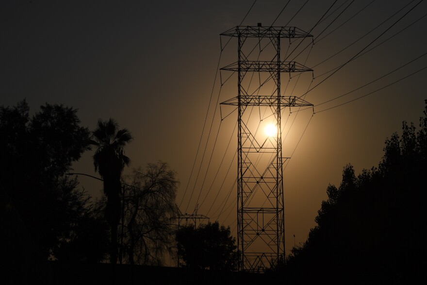 A wide view of a power line tower silhouetted against the sun.