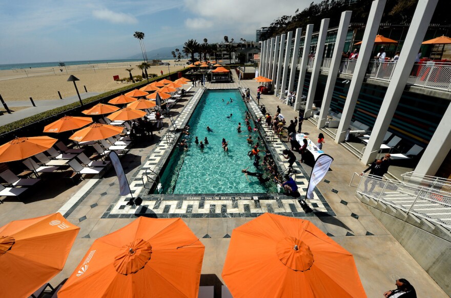 a high-angle shot of a long, rectangular pool surrounded by lounge chairs and orange beach umbrellas