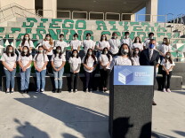 A teenager in a gray shirt speaks at a podium in front of rows of fellow high school students. 