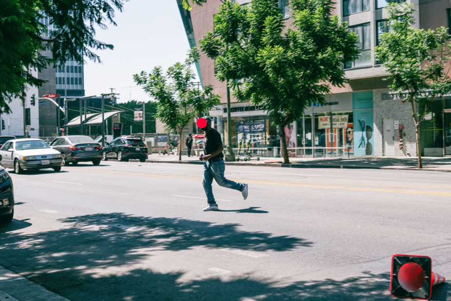 A pedestrian running across a six-lane roadway as a car approaches on his right side.