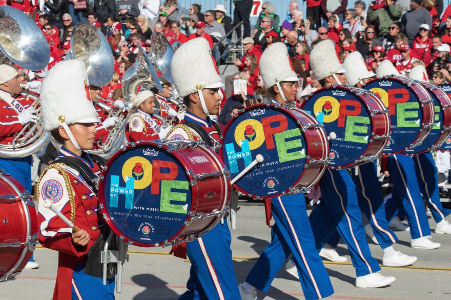 A row of drummers in red and blue uniforms and tall white hats strapped to their chins carry drums reading "HOPE."
