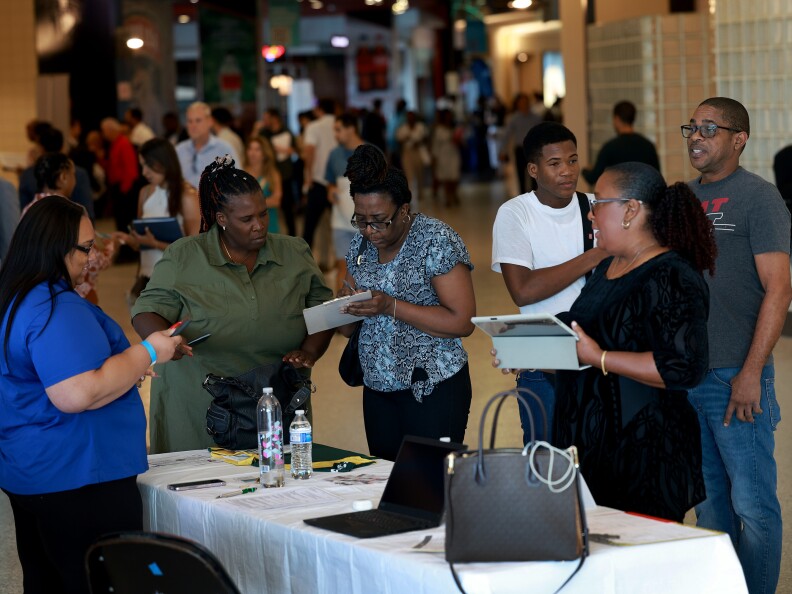 A group of people with dark-tone skin gather around a table filling out forms.