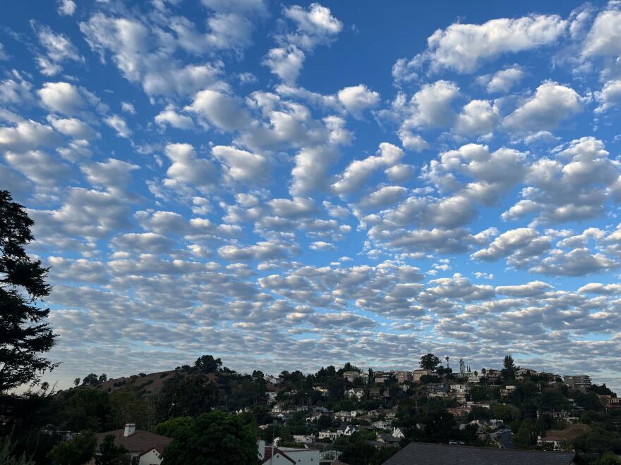 Fluffy clouds in front of blue skies atop a hill of houses.