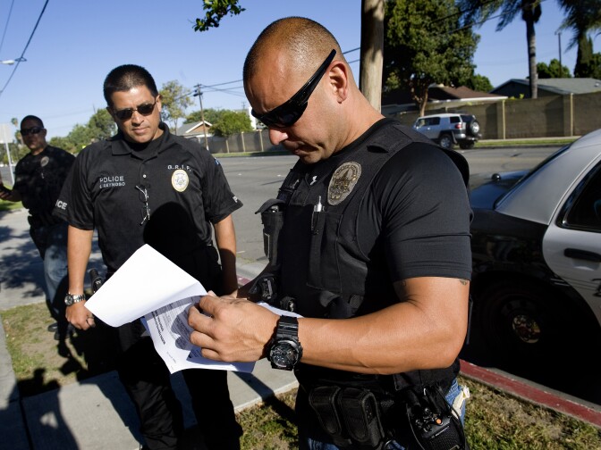 Buena Park police officer James Woo, left, Orange County District Attorney investigator Francisco Reynoso, center, and Buena Park police officer Luis Garcia look over their paperwork before approaching a Buena Park resident who was arrested in a truancy sweep Thursday morning.