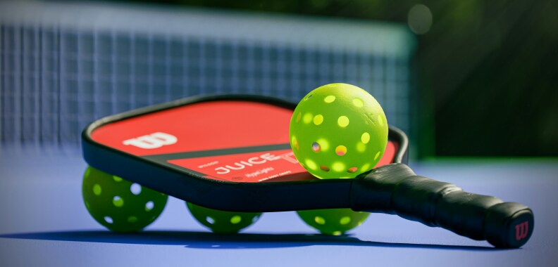 A racket and three lime green balls lie on a pickleball court.