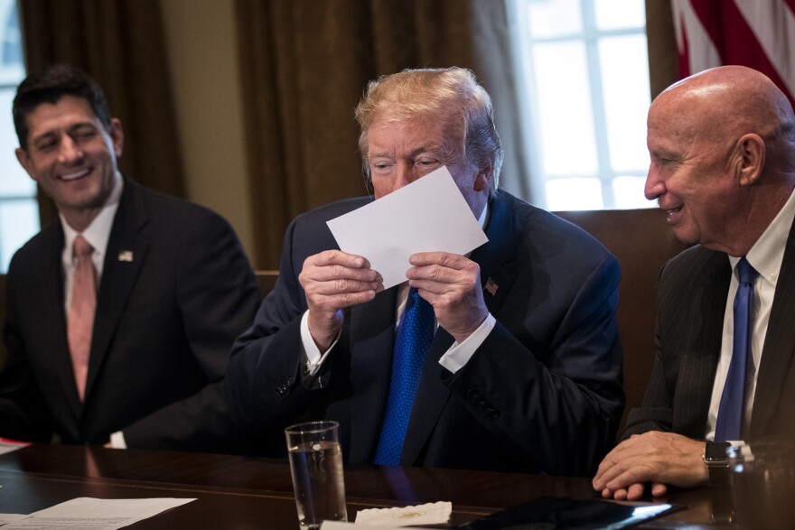 Flanked by Speaker of the House Paul Ryan and House Ways and Means Committee chairman Rep. Kevin Brady (R-TX), President Donald Trump kisses an example of what a new tax form may look like on November 2, 2017.