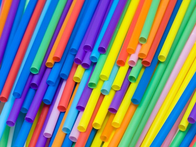 Brightly colored straws thrown around on a table. Some of them are showing the lower side of the tube, with only a few of the flexible heads visible. The colors range from blue to red tones.