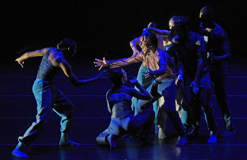 6 people strike dance poses on a dark stage tinged with blue light