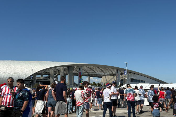 Large crowds of people walk in front of a stadium.