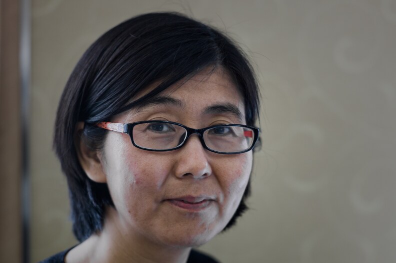 A middle-aged Chinese woman in black glasses and a bob looks at the camera.