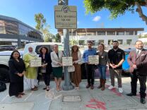 Nine people stand beside a street signed named Jamal Khashoggi Square. Cars and buildings are visible in the background.