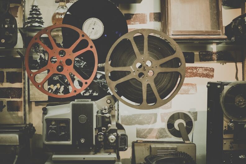 A vintage photograph of film reels, tap recorders, and a vinyl album.