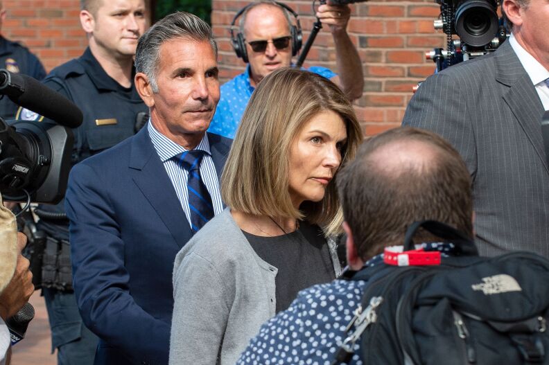 A man in a deep blue suit and woan in a gray sweater set are surrounded by cameras. Both have light-tone skin.
