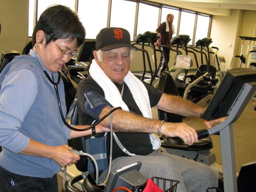 Actor Jonathan Haze bicycles at the Cardiac Rehab Lab at Cedars-Sinai Heart Institute.  Exercise physiologist Asako Oshiro takes his blood pressure while he’s pumping.