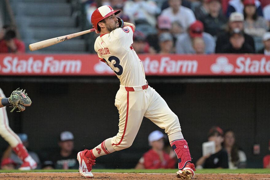 A baseball player in a white and red uniform swings a bat.