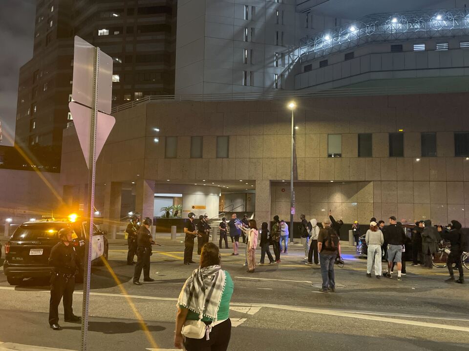 Uniformed officers and people in civilian clothing stand in a street near a jail.