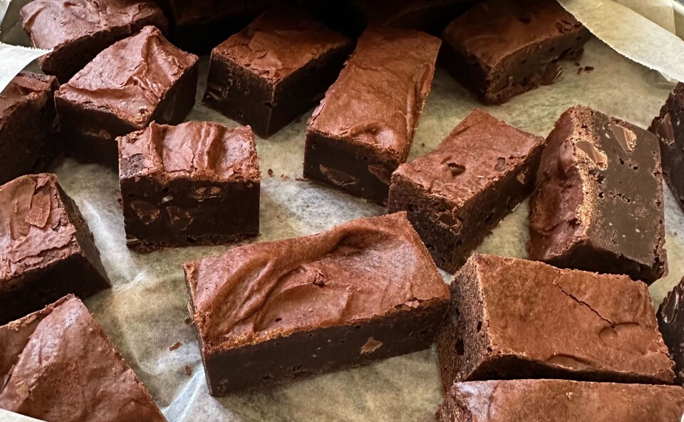 A close up of a pan of brownie squares, deliciously brown and chocolatey, on parchment paper in a pan