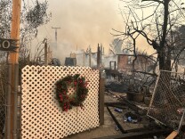 A burned down home with a white fence remaining where a Christmas wreath hangs. 
