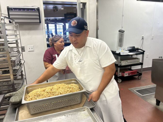 A man in a white apron holds onto a large dish of freshly made spaghetti noodles.