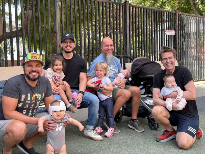 Four light-skinned men pose, smiling, with their young children — four in total, including two babies — at the Silver Lake Recreation Center.