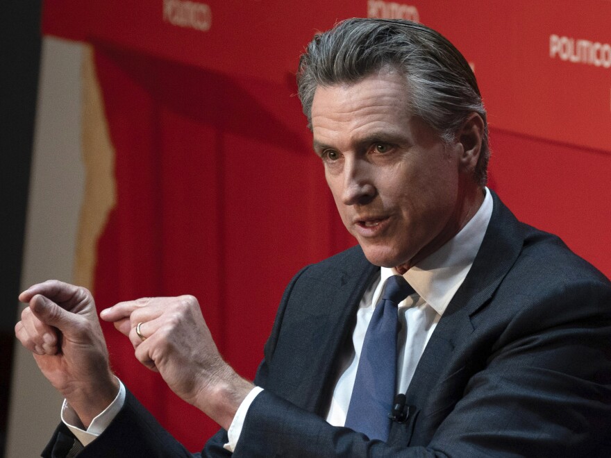 Gov. Gavin Newsom, a man with dark and grey hair wearing a suit, gestures with his hands while speaking during an interview.
