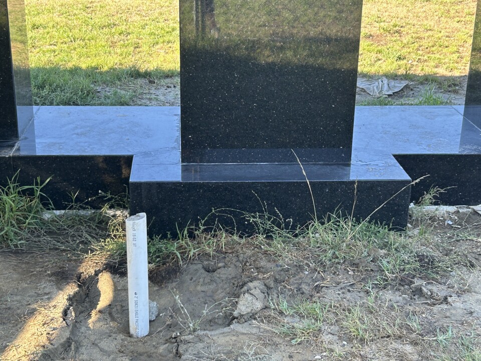 A short white PVC pipe sticks up from muddy ground in front of a black marble-looking platform. 