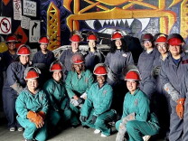 Female presenting people wear red constuction hats, gloves, and thick overalls.