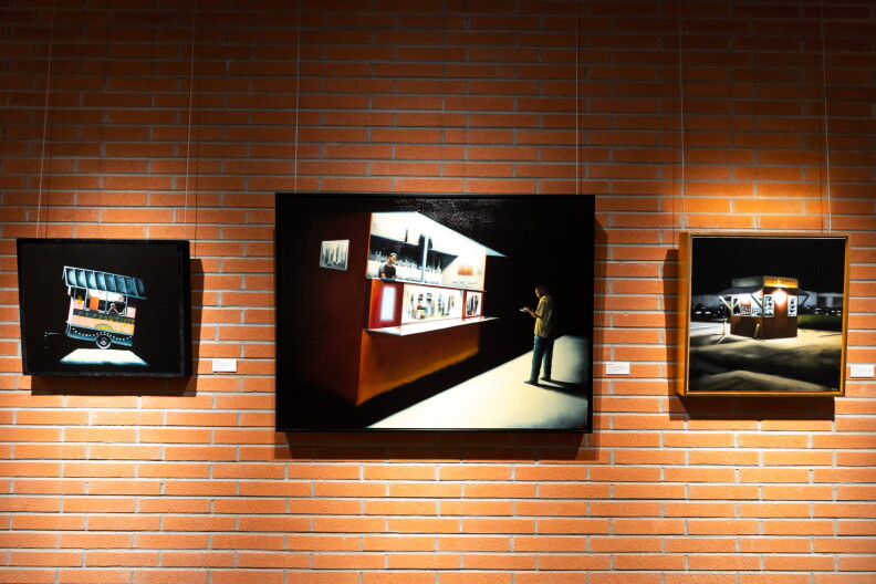 Several paintings with dark backgrounds hang on a brick wall.