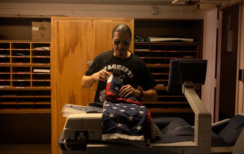 A man in sunglasses folds in American flag in an administrative building.
