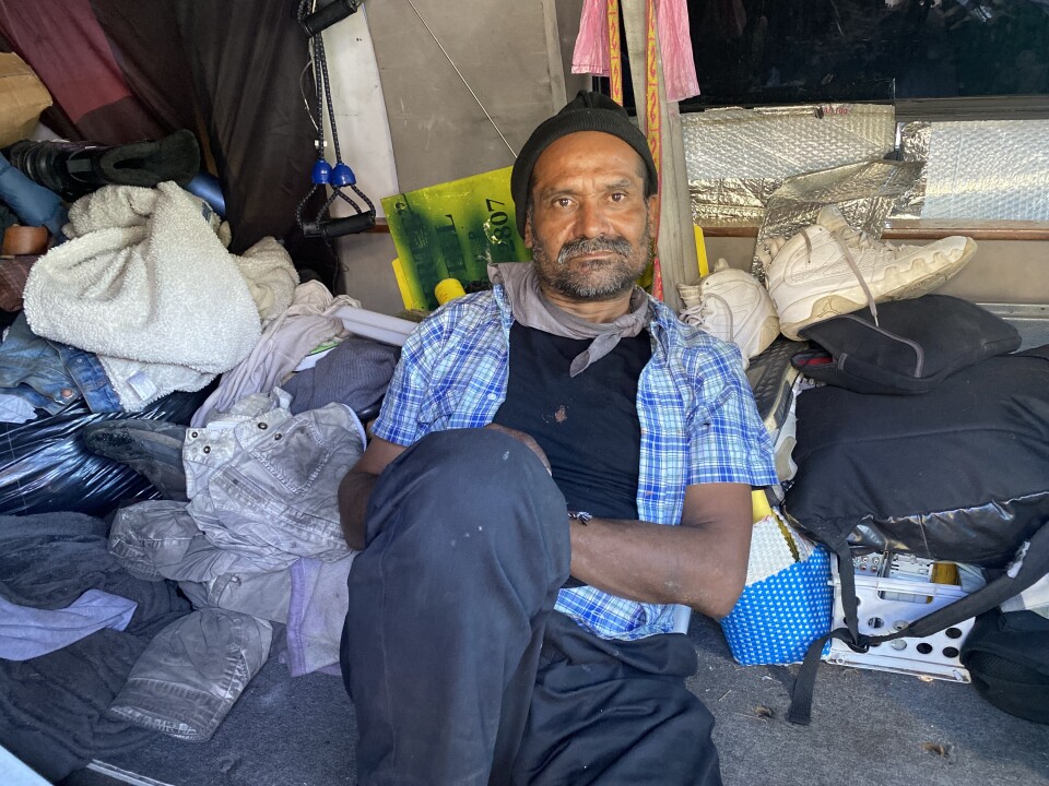 Quentin Rodriguez, who is unhoused, sits on the floor of his camper van surrounded by his belongings.