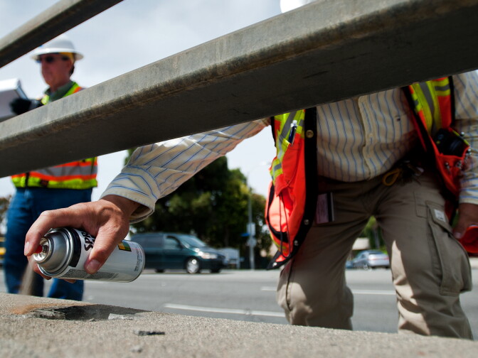 Wu spray paints circles around small chips in the concrete railing on the Manhattan Beach bridge, to mark them for future repairs.