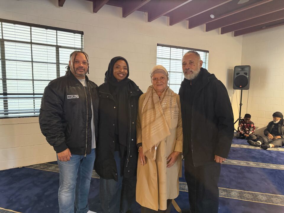 Four people: one in a black leather jacket and jeans, another in a black coat and black hijab, one wearing a beige coat and beige hijab and another in a black coat and pants, look ahead at the camera. 