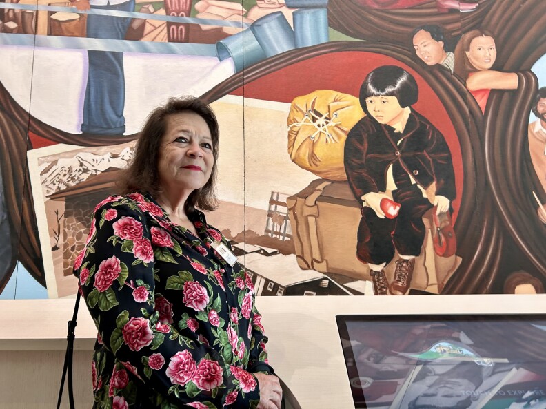 Person with medium skin tone wearing a top with flowers, standing in front of a painting of a child.