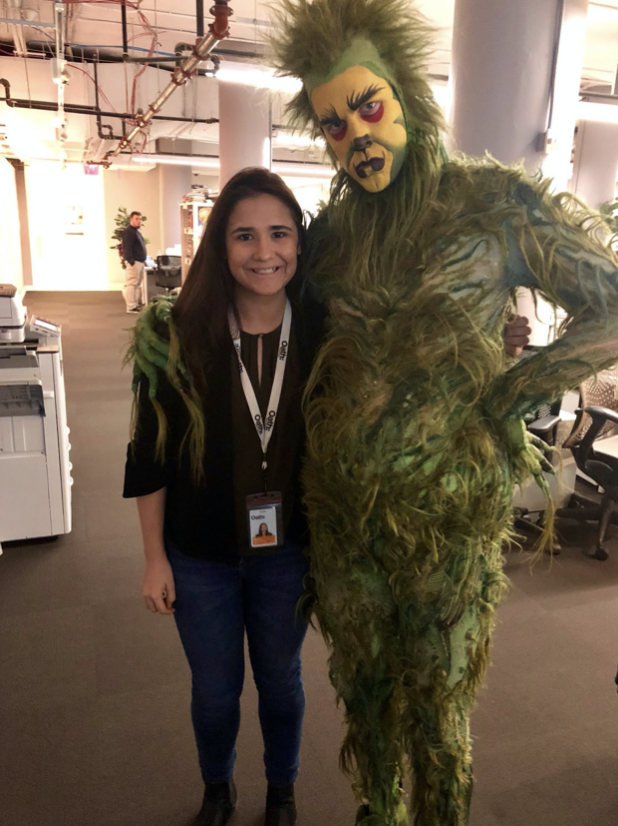 A costumed green Grinch has an arm around Marina Peña's right shoulder in the Yahoo! Finance newsroom.