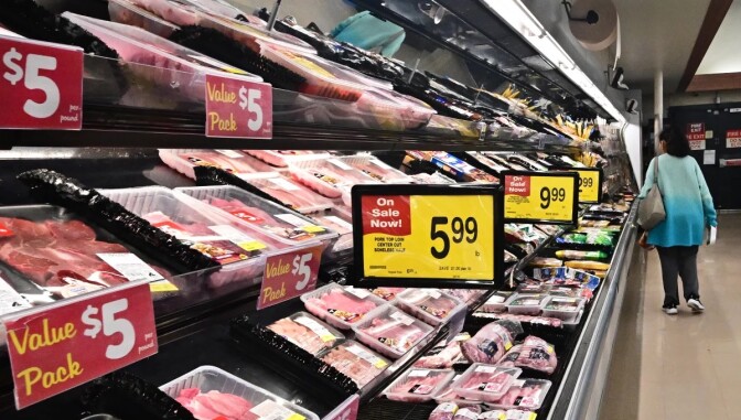 A photo of a meat aisle in a grocery store with a person in a blue sweater 