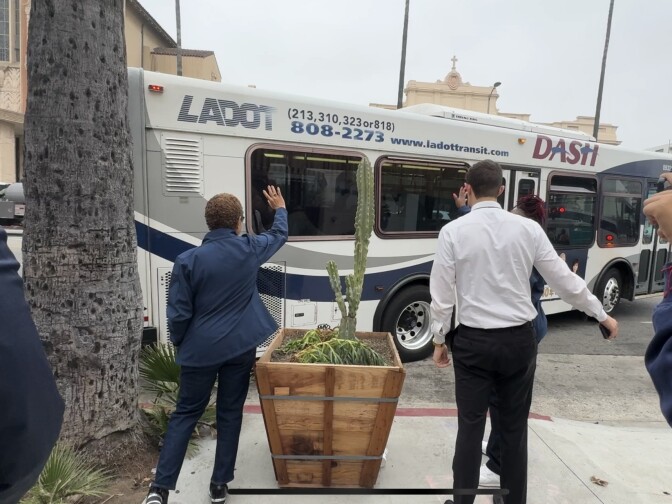 A woman waves to a departing bus that has "LADOT" written on the side.