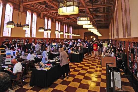 A library hall is filled with table and vendors presenting archival work to patrons.