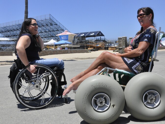 Tiffany Giddes, left, introduced herself to Kim Berger, right, of Modesto while they were both rolling along a path adjacent to Huntington Beach. Berger borrowed a "beach chair" for free from a food concession stand for the day. Its extra-wide wheels allow her to roll across the sand without sinking. 