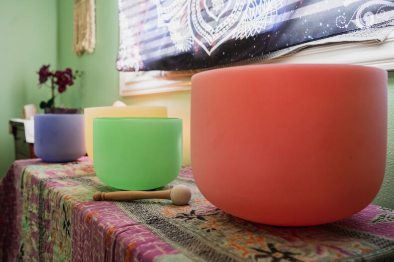 Colorful singing bowls in red, green, yellow, and blue sit on a table with a decorated tablecloth.