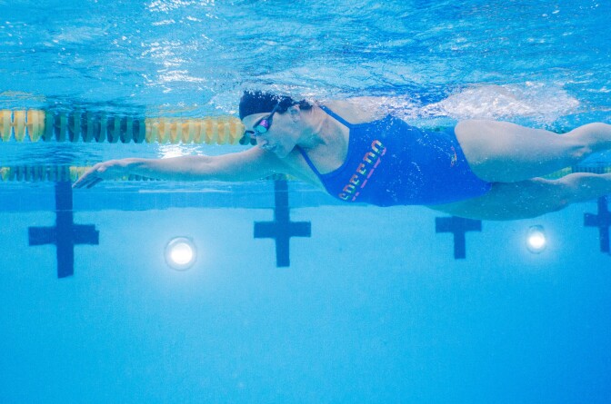 Clad in a bathing suit, swim cap and goggles, a woman swims underwater in a pool. 