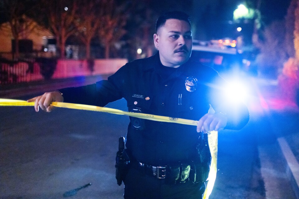 A uniformed officer pulls police tape across a street.