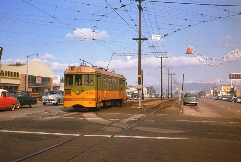 An image from 1955 shows old cars on a wide road with a gold and green streetcar running on tracks at the center.