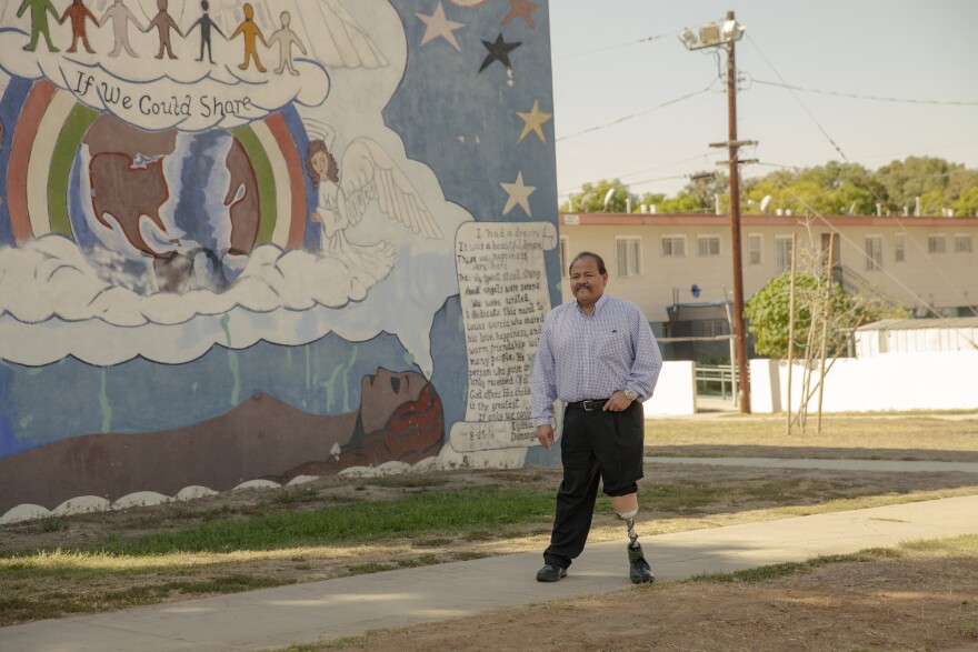A man with a prosthetic left leg walks past a building with a colorful mural with a message that says "If We Could Share."