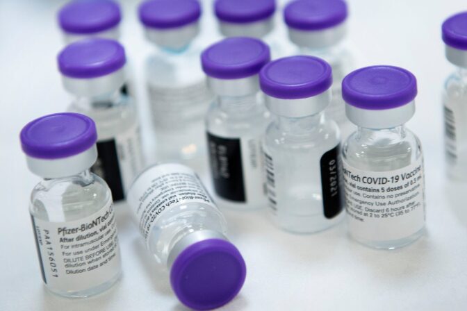 A close up of 10 small vials with purple caps that have the COVID-19 vaccine in them.
