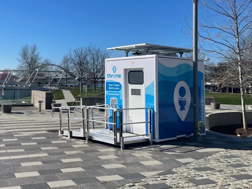 A public restroom with a wheelchair-accessible ramp and a solar panel is located in a public plaza.