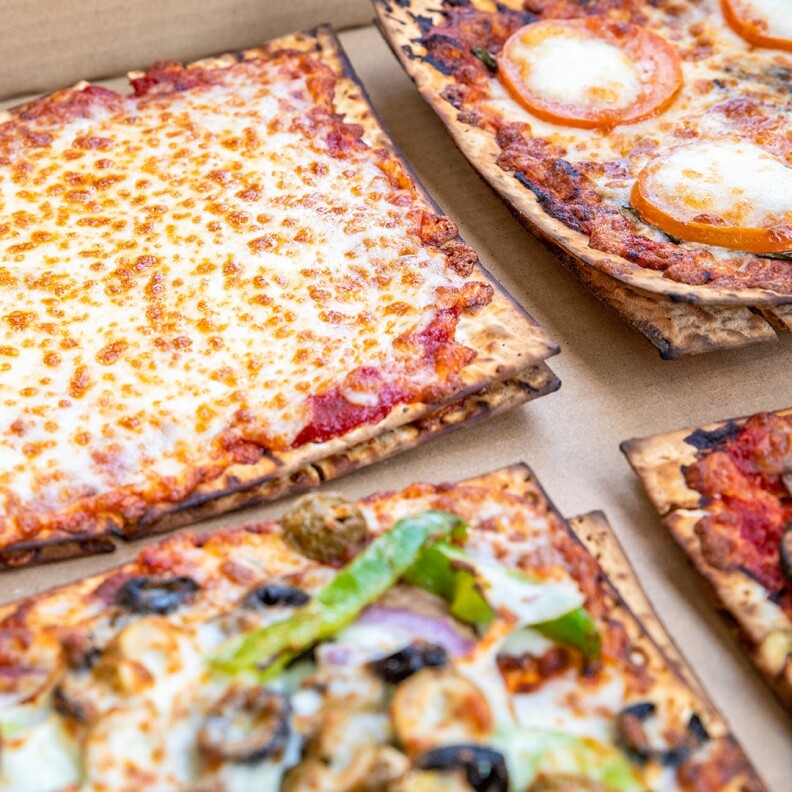 A close up shot of four matzah pizza with different toppings against a cardboard background