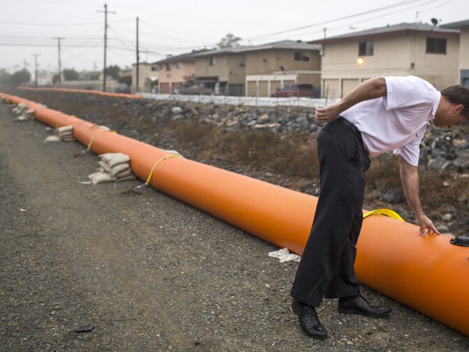Shannon Widor, a communications officer for Orange County Public Works stands over a water-inflatable Tiger Dam at the Carbon Creek Channel in Anaheim on Thursday morning, Dec. 10, 2015.