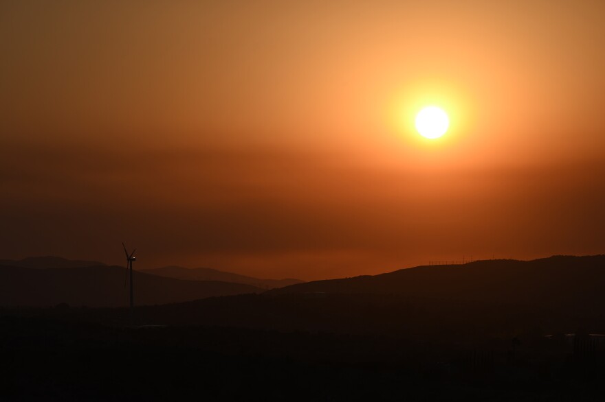 A hot orange sun hangs in the sky over silhouetted hills