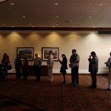 Job seekers read pamphlets as they wait in line to enter a job fair.