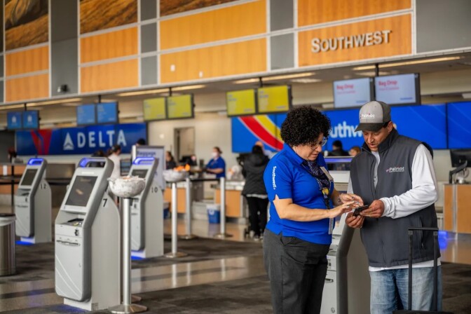 A person wearing a blue Southwest top helps someone wearing a grey pullover in a check-in area at an airport. 